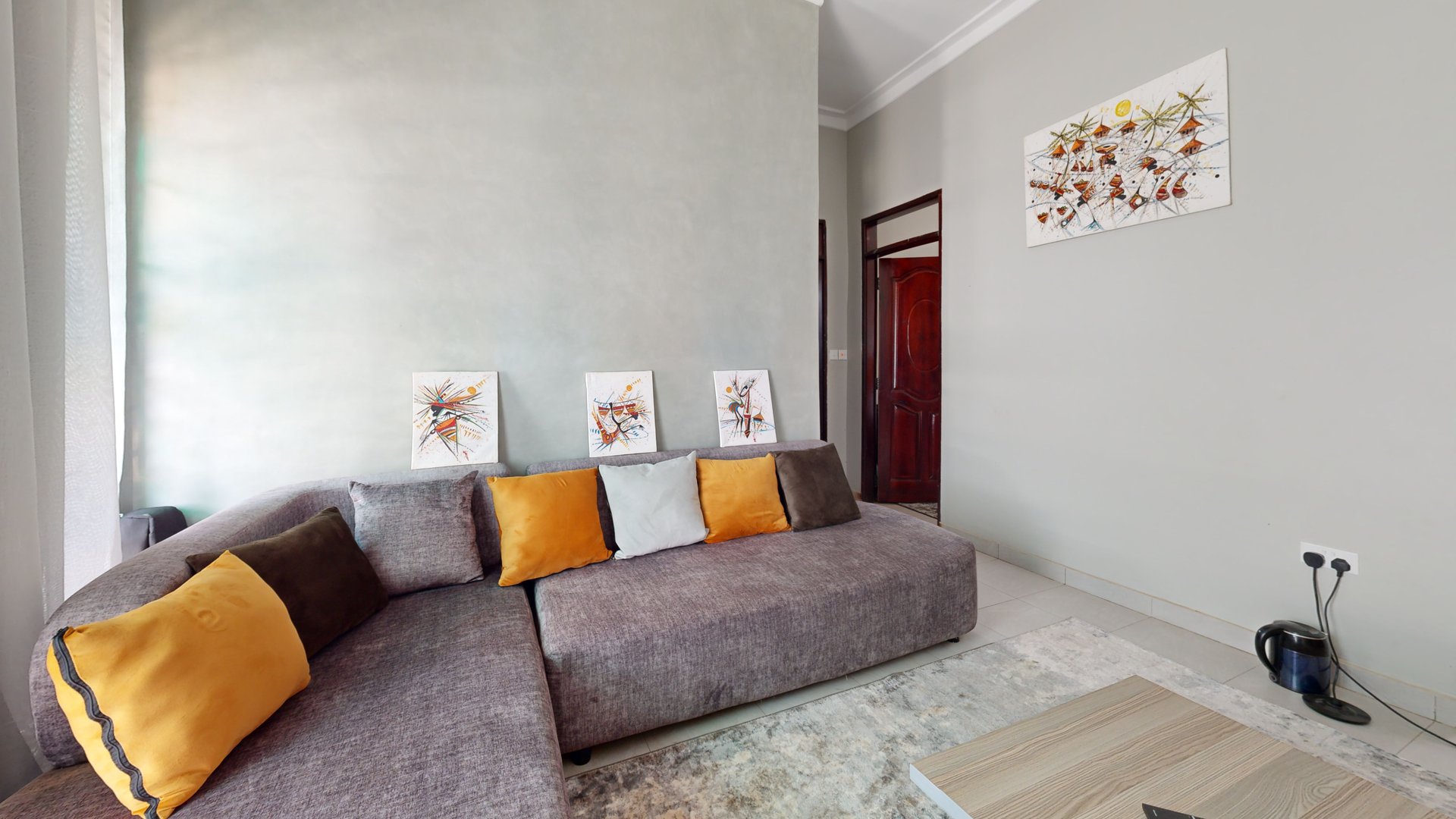 Living room inside Matwale Airbnb with a grey sofa and yellow cushions